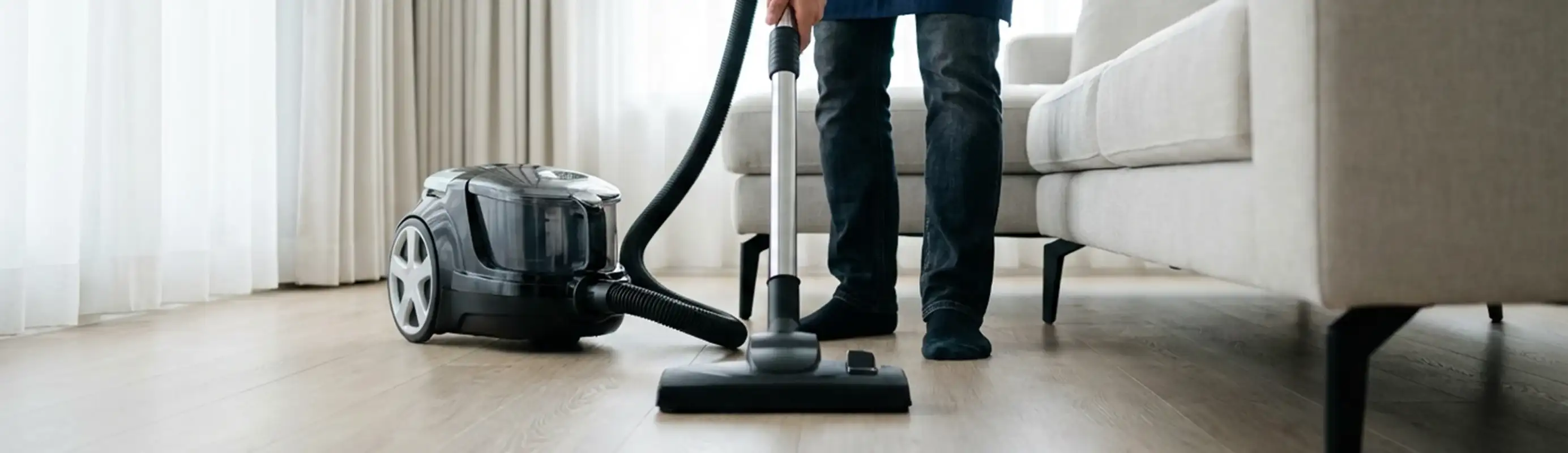 Professional house cleaner vacuuming a living room floor with a canister vacuum cleaner, New Haven, CT.