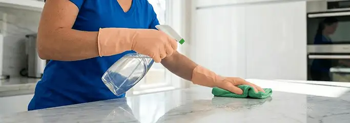 Maid service worker spraying and wiping a kitchen countertop with a microfiber cloth for sanitizing, New Haven, CT.
