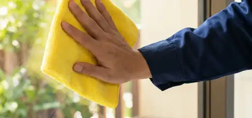 House cleaner wiping a glass window with a yellow microfiber cloth for streak-free cleaning, New Haven, CT.